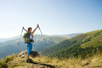 Una mujer levanta los brazos con bastones en sus manos tras coronar una montaña